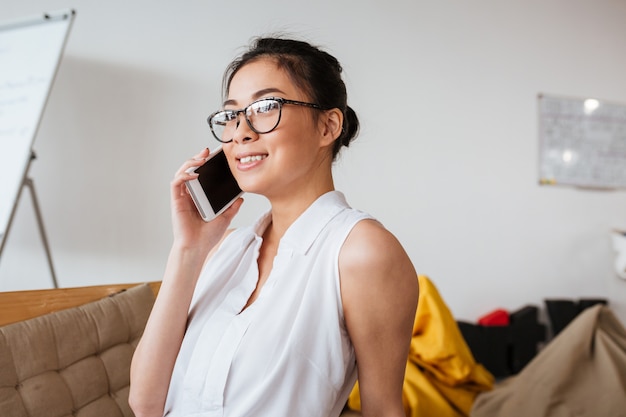 Het glimlachen van leuke jonge vrouwenzitting en het spreken op celtelefoon