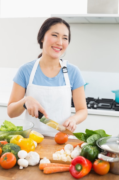 Het glimlachen van vrouwen hakkende groenten in keuken