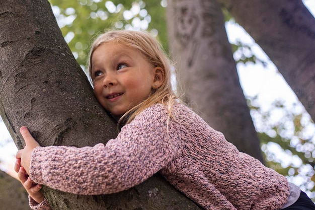 Het glimlachende blonde meisjeskind ligt een boom met twee handen te koesteren