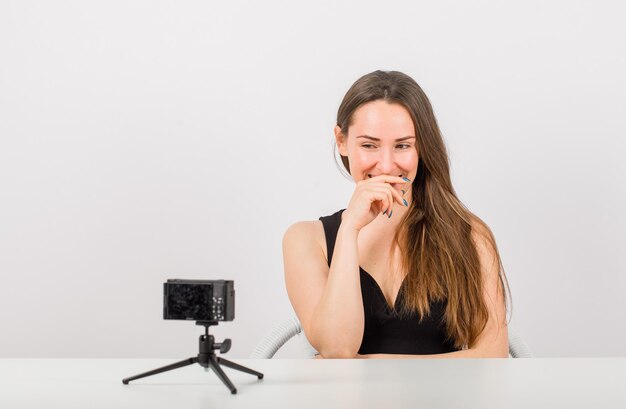 Het glimlachende jonge meisje stelt bij kleine camera door hand op mond op witte achtergrond te houden