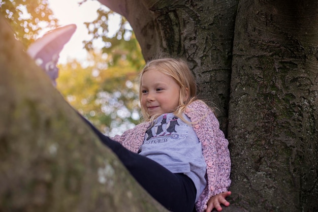 Het glimlachende kindmeisje speelt zittend hoog op een boom in het park