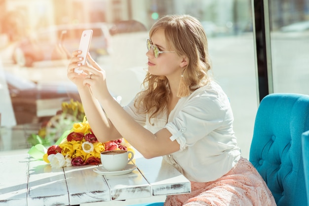 Het glimlachende meisje maakt een selfie zittend op het terras van het café