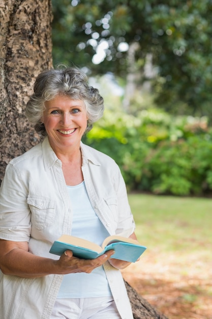 Het glimlachende rijpe boek die van de vrouwenlezing op boomboomstam leunen