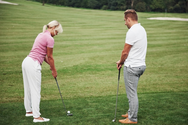 Het golf van het meisje en het raken door putter op groen. Haar leraar helpt om de techniek te verkennen en haar eerste stakingen te maken