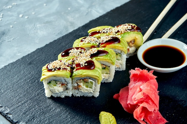 Het groene broodje van drakensushi met avocado, paling, Philadelphia-kaas en unagisaus op een zwarte leiraad.