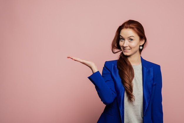 Het horizontale portret van gelukkig vrouwelijk model geeft met palm aan op lege exemplaarruimte, toont plaats voor uw advertentie of promotietekst. Vrouw tonen die op roze muur richten