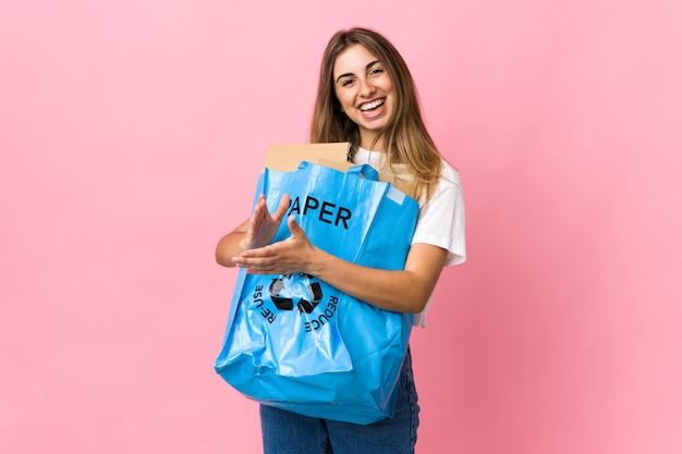 Het houden van een recycling zak vol papier te recyclen over geïsoleerde roze applaudisseren