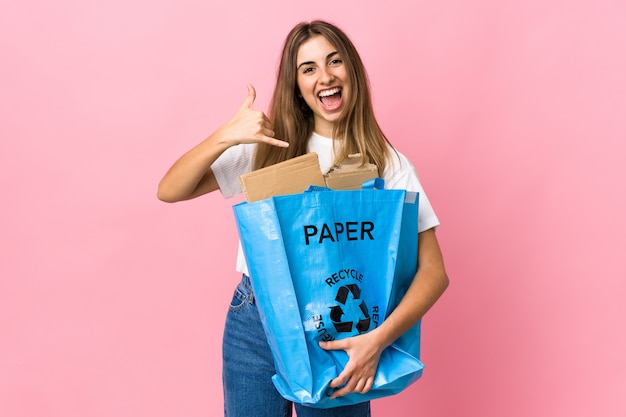 Het houden van een recycling zak vol papier te recyclen over geïsoleerde roze telefoon gebaar maken