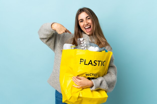 Het houden van een zak vol plastic flessen om te recyclen over geïsoleerde blauw met verrassing gezichtsuitdrukking