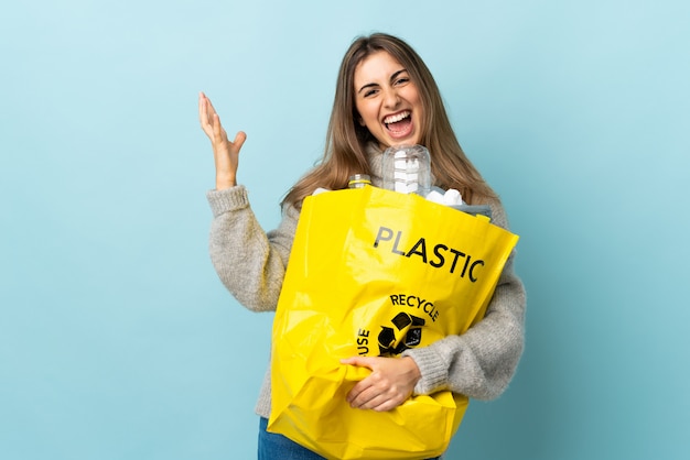 Het houden van een zak vol plastic flessen te recyclen op geïsoleerde blauw ongelukkig en gefrustreerd met iets