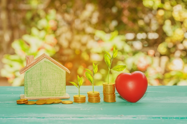 Het huismodel met rood hart en kweekt kleine installatiesstapel muntstukken op aardachtergrond. Property conce.