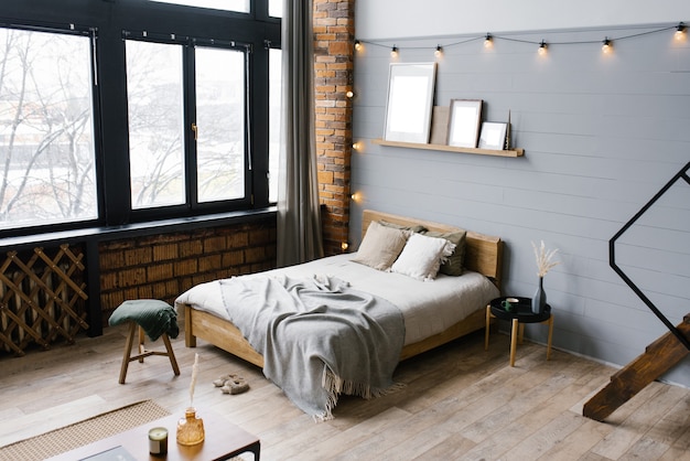 Het interieur van de slaapkamer is in een moderne Scandinavische stijl met grijze houten en bakstenen muren, een comfortabel tweepersoonsbed, een panoramisch raam