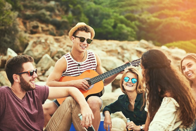 Het is altijd een plezier om voor jullie te spelen Shot van een jonge man die gitaar speelt voor zijn vrienden terwijl hij aan het chillen is op het strand