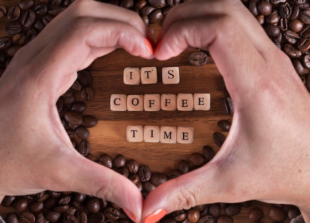 Het is koffietijd met een houten kubusletters en een vrouw die een hart maakt met haar handen