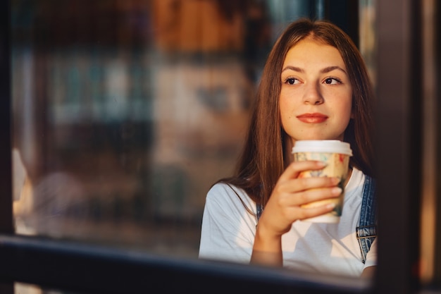 Het jonge aantrekkelijke mooie meisje bij koffie met koffie ontspant bij ochtend throuth glas