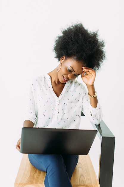 Het jonge Afrikaanse Amerikaanse bedrijfsvrouw typen op laptop terwijl het zitten op de stoel, op wit wordt geïsoleerd dat