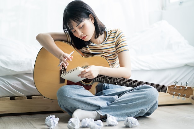 Het jonge Aziatische meisje oefent thuis gitaar en componeert muziek