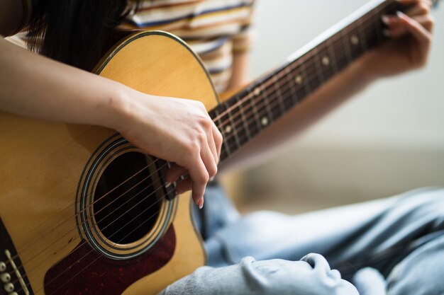 Het jonge Aziatische meisje oefent thuis gitaar en componeert muziek