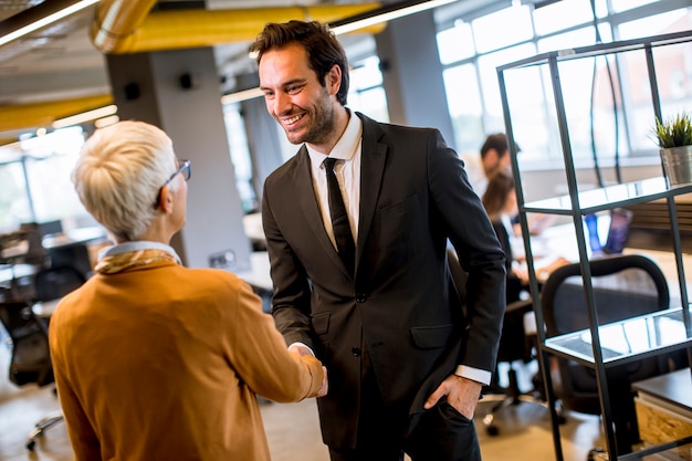 Het jonge bedrijfsman en hogere bedrijfsvrouwen schudden dient het bureau in