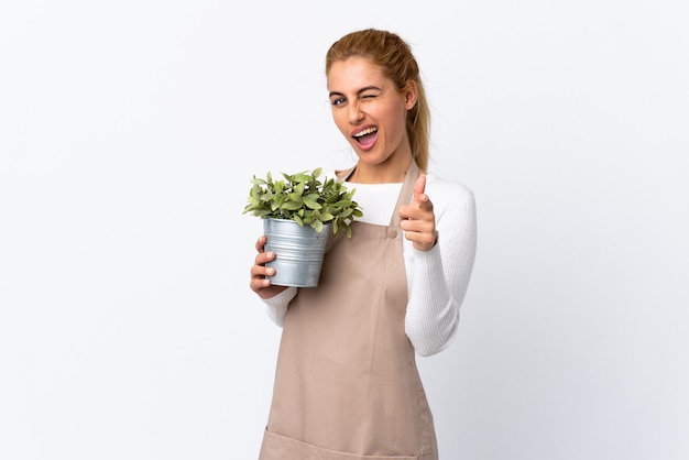 Het jonge blonde meisje dat van de tuinmanvrouw een installatie over witte muur houdt richt vinger