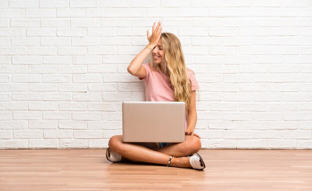 Het jonge blonde studentenmeisje met laptop op de vloer die twijfels hebben met verwart gezichtsuitdrukking