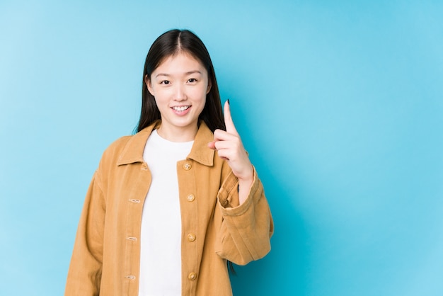 Het jonge Chinese vrouw stellen in een blauwe muur die nummer één met vinger tonen.