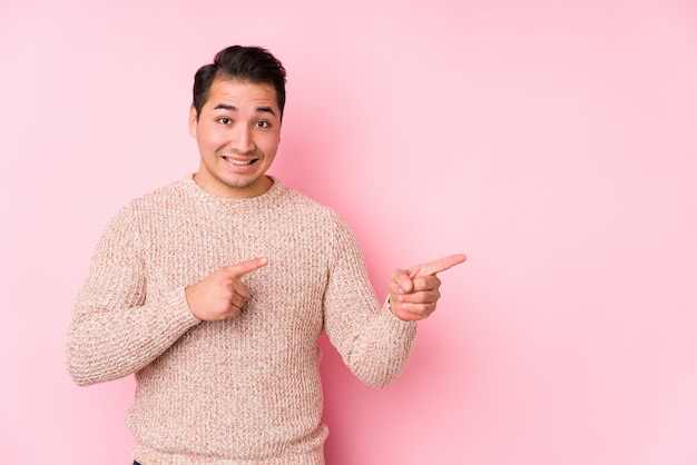 Het jonge curvy mens stellen in een roze muur isoleerde geschokt wijzend met wijsvingers aan een exemplaarruimte.