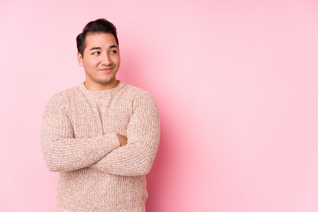 Het jonge curvy mens stellen in een roze muur isoleerde glimlachend zeker met gekruiste wapens.