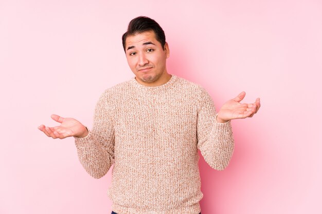 Het jonge curvy mens stellen in een roze muur isoleerde twijfelende en schouderophalend schouders in vragend gebaar.