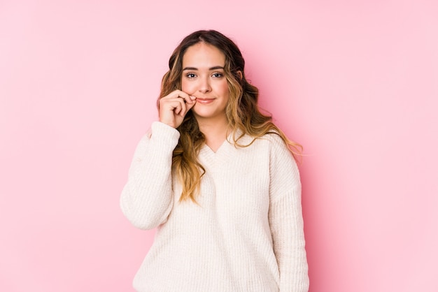 Het jonge curvy vrouw stellen in een roze muur die met vingers op lippen wordt geïsoleerd die een geheim houden.