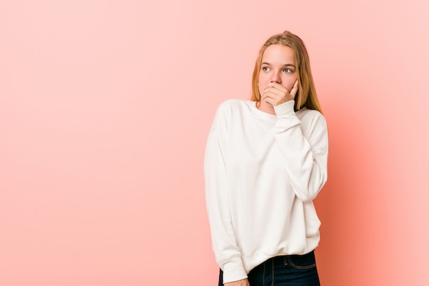 Het jonge de vrouw van de blondetiener nadenkende kijken aan een exemplaarruimte die mond behandelen met hand.