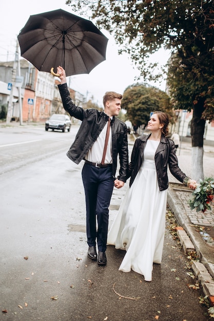 Het jonge gelukkige paar loopt op een stadsstraat na regen. Close-upportret van een man en een vrouw met een paraplu. Verliefde paar glimlachend buitenshuis. Een man loopt over straat en zwaait met een paraplu