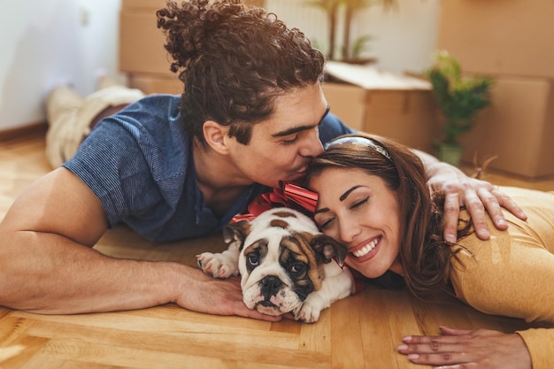 Het jonge gelukkige paar verhuist naar een nieuw huis. ze liggen op de grond met hun kleine puppy nadat ze dozen met spullen naar hun nieuwe huis hebben gebracht.