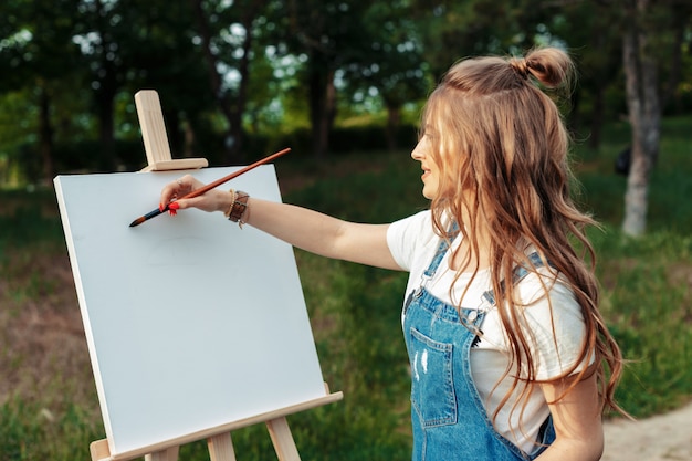 Het jonge Kaukasische vrouw schilderen op canvas buiten