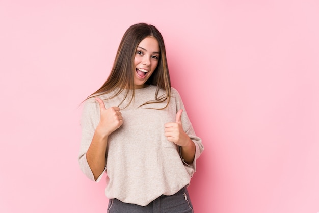 Het jonge Kaukasische vrouw stellen geïsoleerd opheffend beide duimen omhoog, glimlachend en zeker.