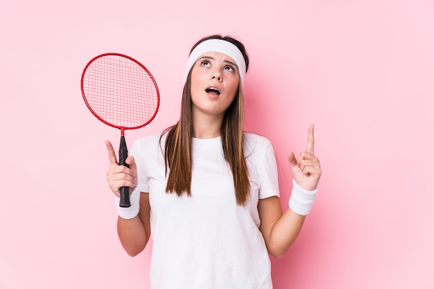 Foto het jonge kaukasische vrouwen speelbadminton isoleerde richtend bovenkant met geopende mond.