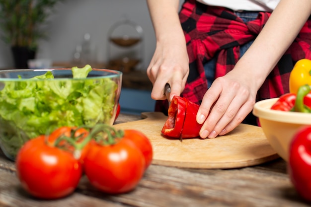 Het jonge meisje bereidt een vegetarische salade in de keuken voor, hakt zij peper, het proces om gezond voedsel, close-up voor te bereiden