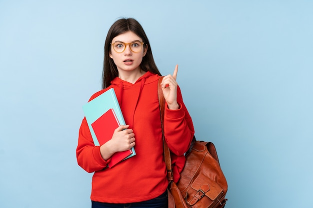 Het jonge meisje dat van de tienerstudent een salade over blauwe muur houdt verrast en vinger aan de kant richt