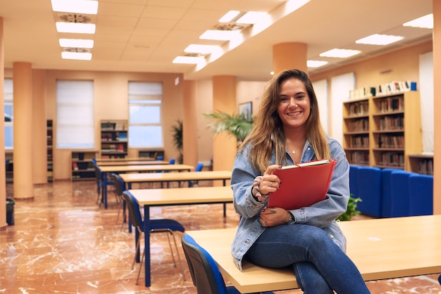 Het jonge meisje glimlachen kijkt in de camera met de lege bibliotheek