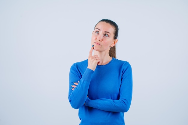 Het jonge meisje kijkt omhoog door wijsvinger op de lippen op een witte achtergrond te leggen