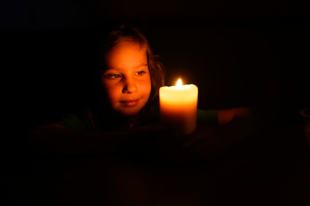 Het jonge meisje van zeven jaar bewondert thuis een brandende kaars in de avond