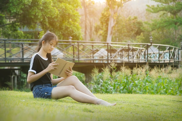 Het jonge meisje zit op gras en leest boek