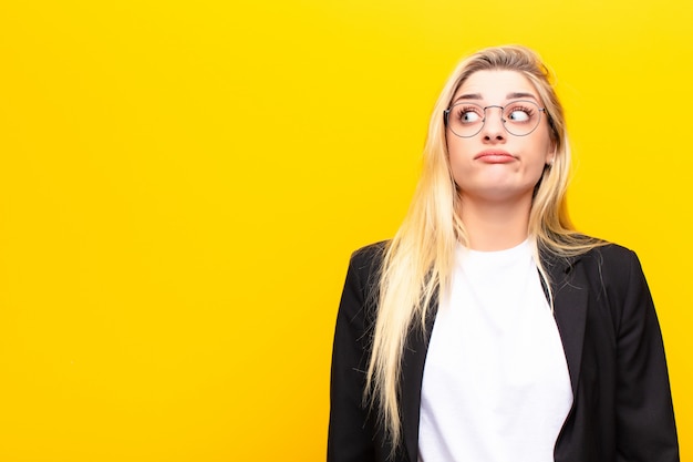 Het jonge mooie blondevrouw benieuwd zijn, denkend gelukkige gedachten en ideeën, dagdromen, die ruimte aan kant tegen gele muur kijken te kopiëren