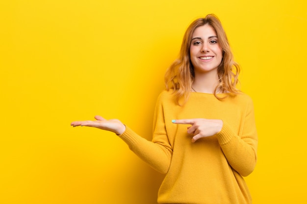 Het jonge mooie blondevrouw glimlachen die aan kant tegen gele muur richten