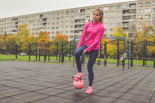 Het jonge mooie meisje doet sportoefeningen kettlebell fitness buiten