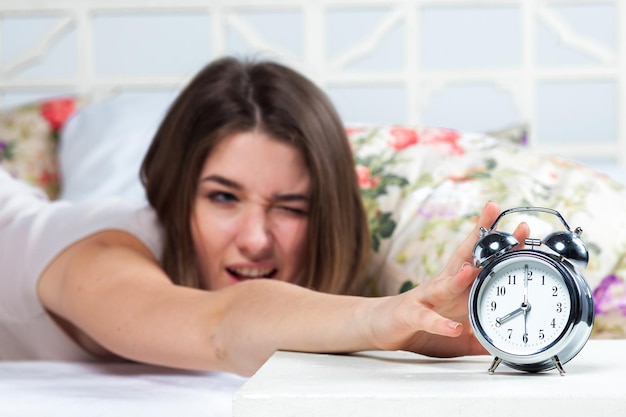 Het jonge mooie meisje in bed. De klokkenservice staat op de voorgrond