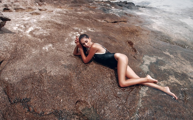 Het jonge mooie meisje in een zwart gesloten zwempak ontspant en zonnebaadt op het strand in Thailand in Phuket
