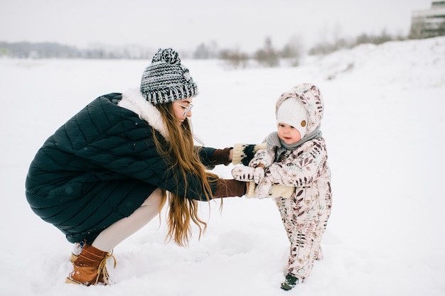 Het jonge mooie moeder spelen met weinig dochter openlucht in de winter. Het gelukkige vrolijke glimlachende wijfje met mooi kind heeft pret in sneeuw. Moederschap en jeugd.