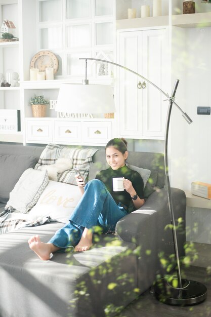 Foto het jonge mooie vrouw ontspannen op bank thuis en het gebruiken van slimme telefoon