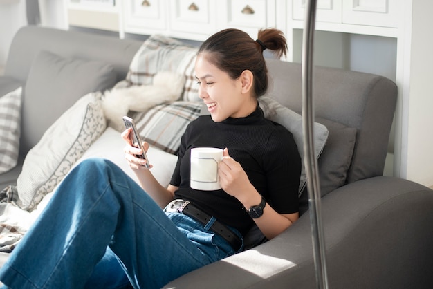 Het jonge mooie vrouw ontspannen op bank thuis en het gebruiken van slimme telefoon